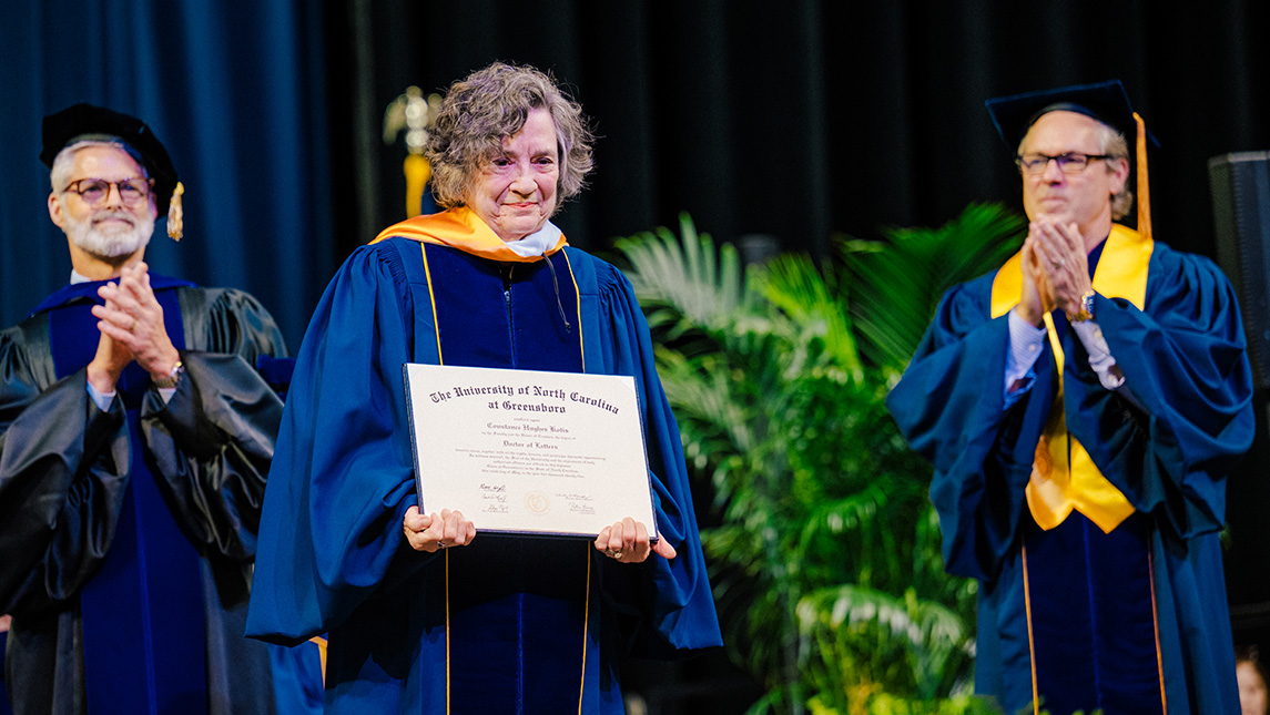 Connie Kotis holds up honorary degree at UNCG Commencement.