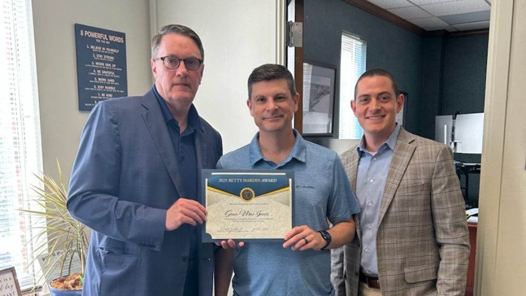 UNCG's Sean MacInnes holds up his award certificate alongside Vice Chancellor Bob Shea and AVC Zach Smith.