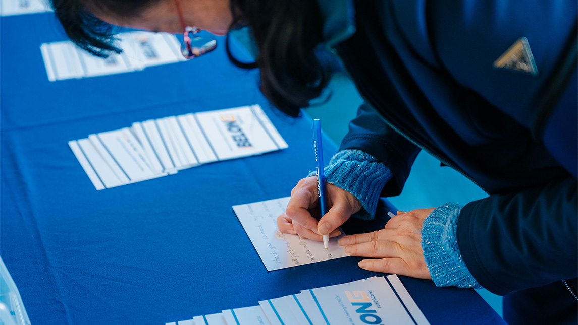 A person writes on a message on a postcard at a UNCG iBelong event.