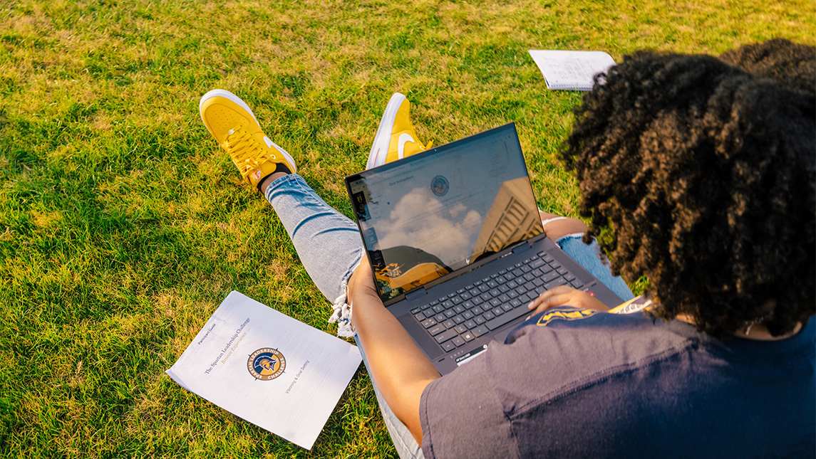 Sun reflects off the screen of a UNCG student's laptop while sitting out on the lawn.
