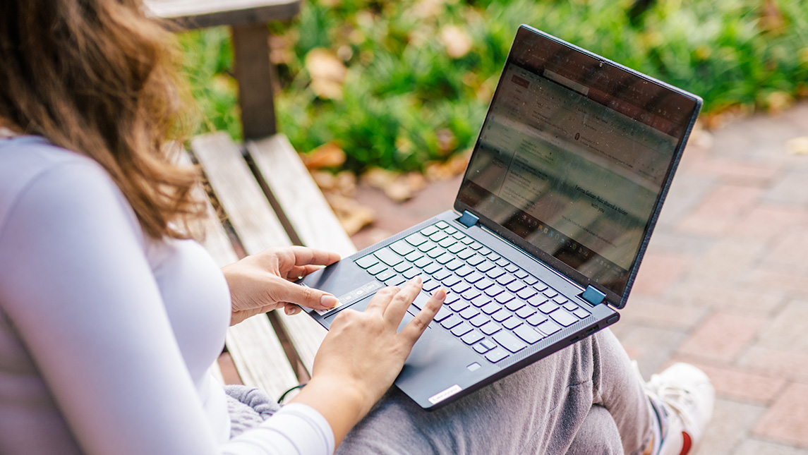 A UNCG student sitting on a bench types on a laptop.