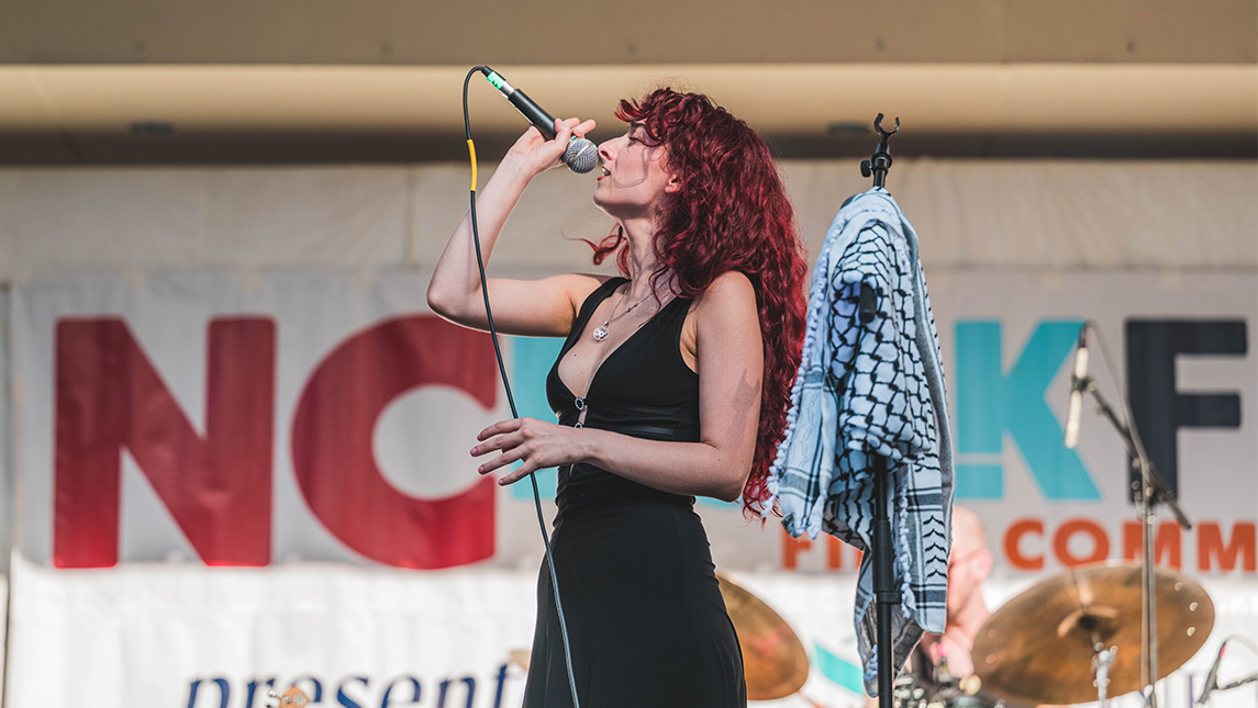 Singer holds a mic on an NC Folk Fest stage.