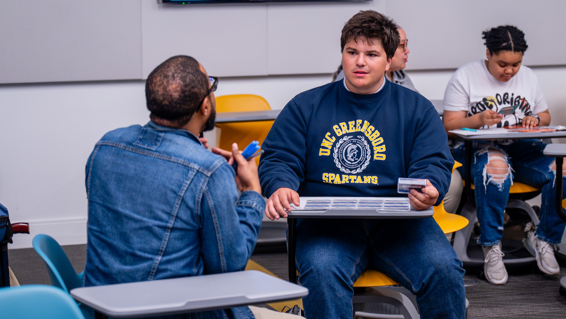 Two people talk in a UNCG classroom.