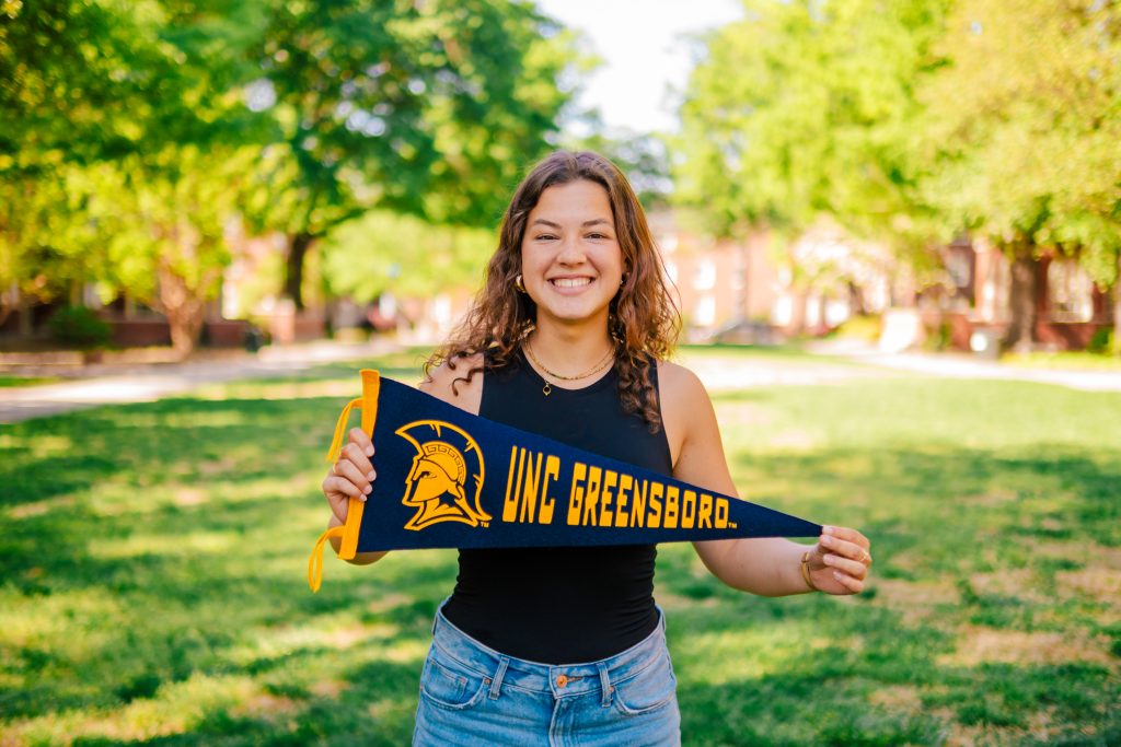 Student holds a UNCG penant in the quad.