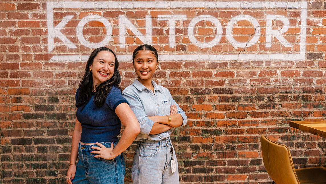 UNCG alumni Ana Mena and Marya Sorn stand back to back in front of a Kontoor sign.
