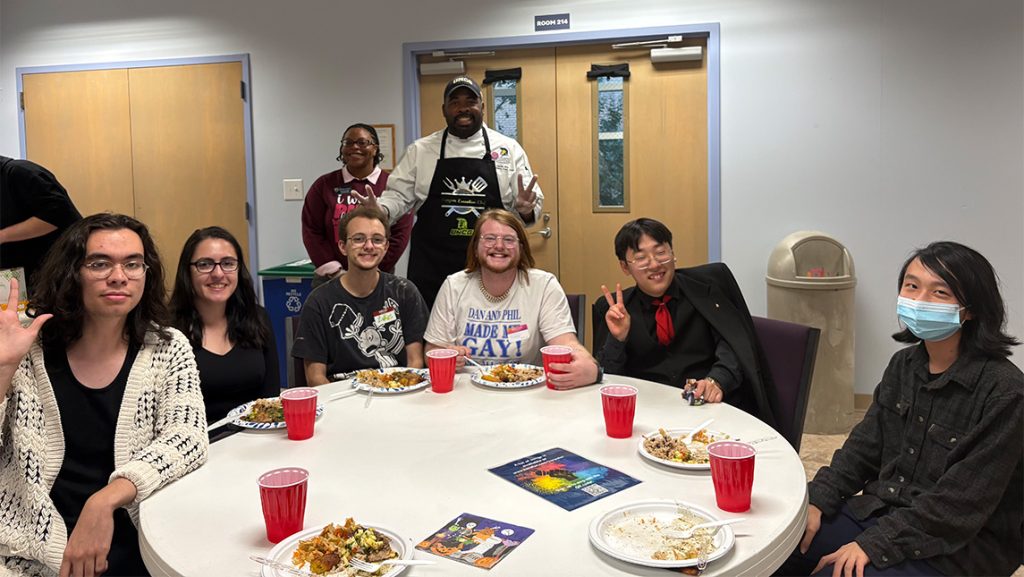 People eating around a table with a UNCG Chef Darelle behind them.