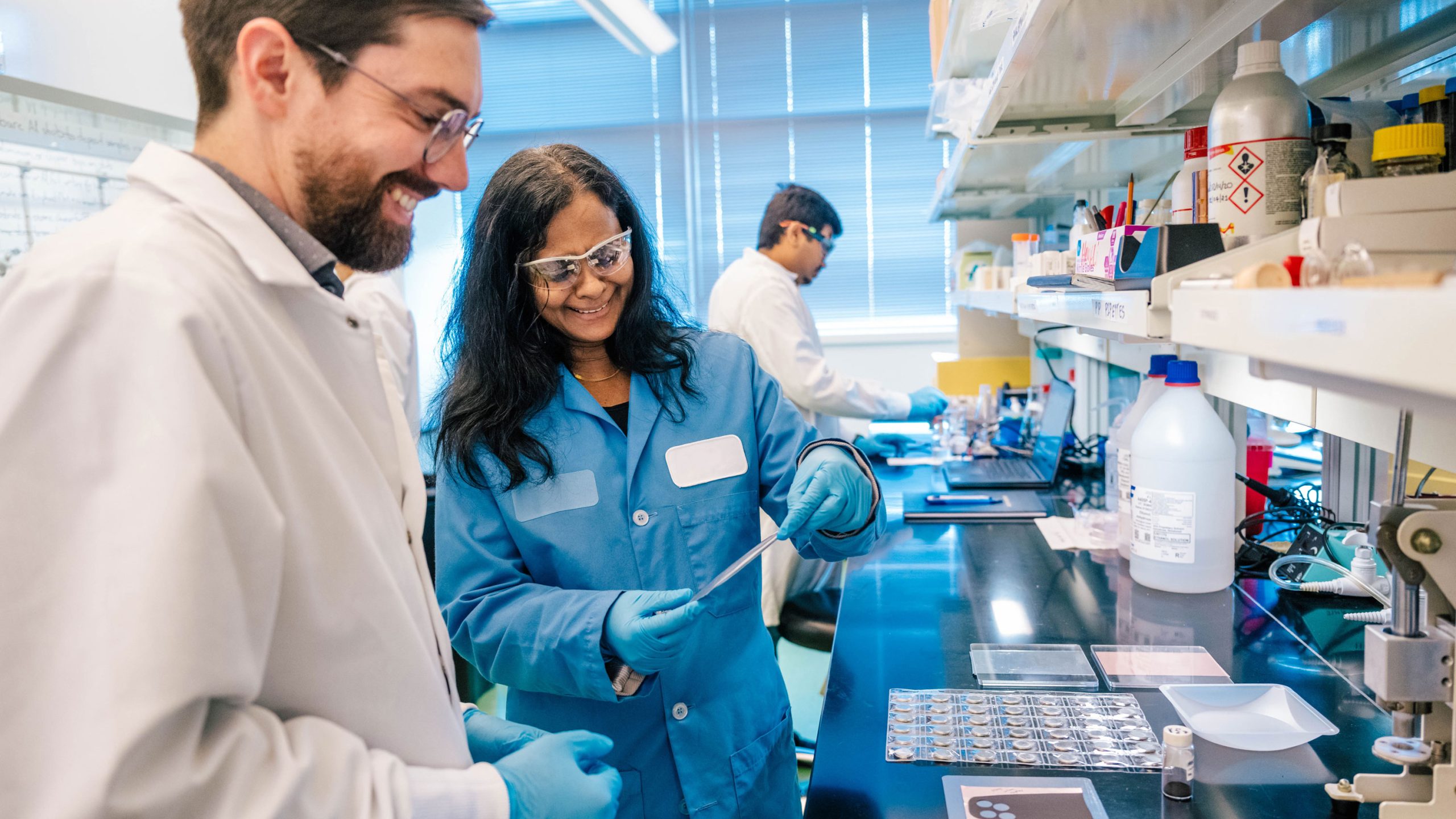 Man and woman in lab coats fabricating batteries