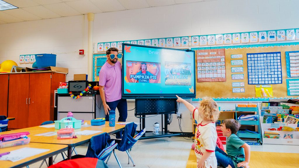 A teacher in big sunglasses makes children laugh.