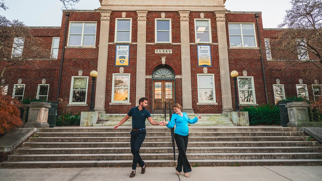 A man and a woman dance in front of the Curry education building on UNCG campus.