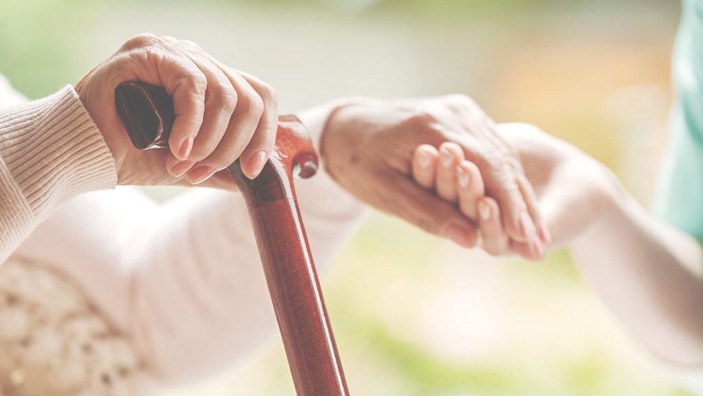 Close-up on a young hands holding older hands with a cane.