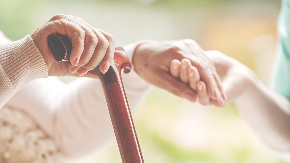 Close-up on a young hands holding older hands with a cane.