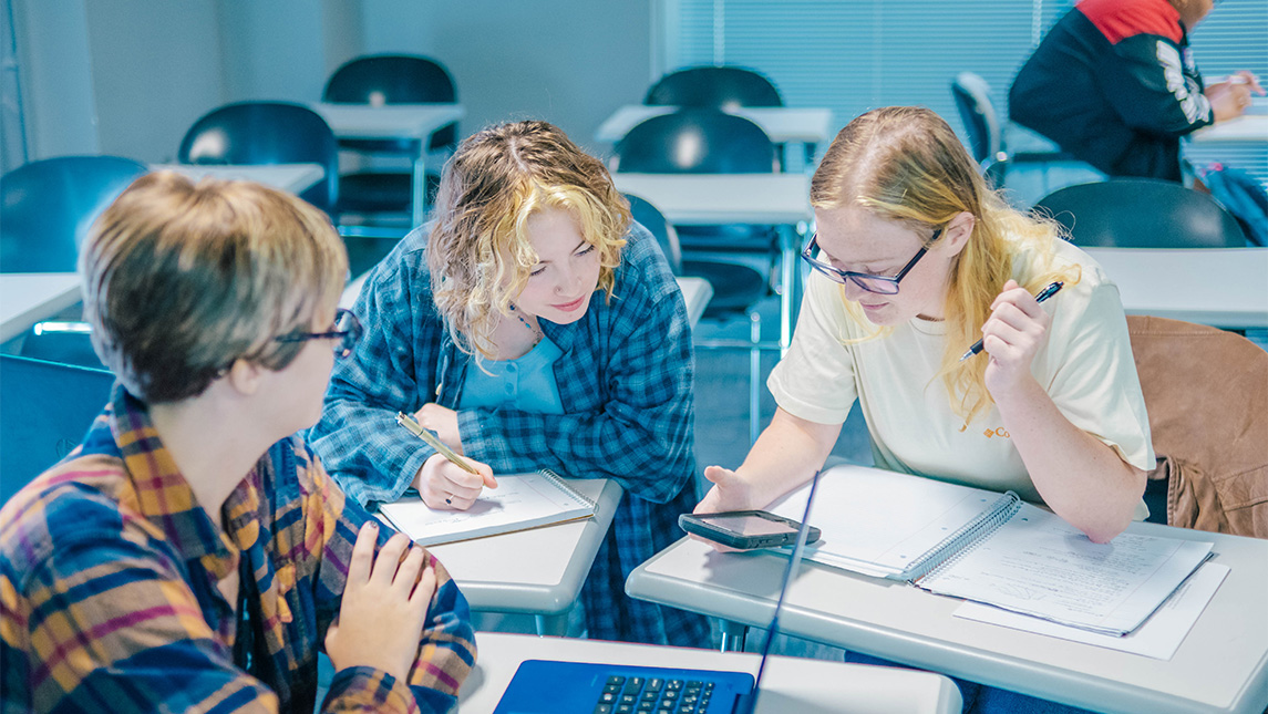 Students look over notebooks in a classroom.