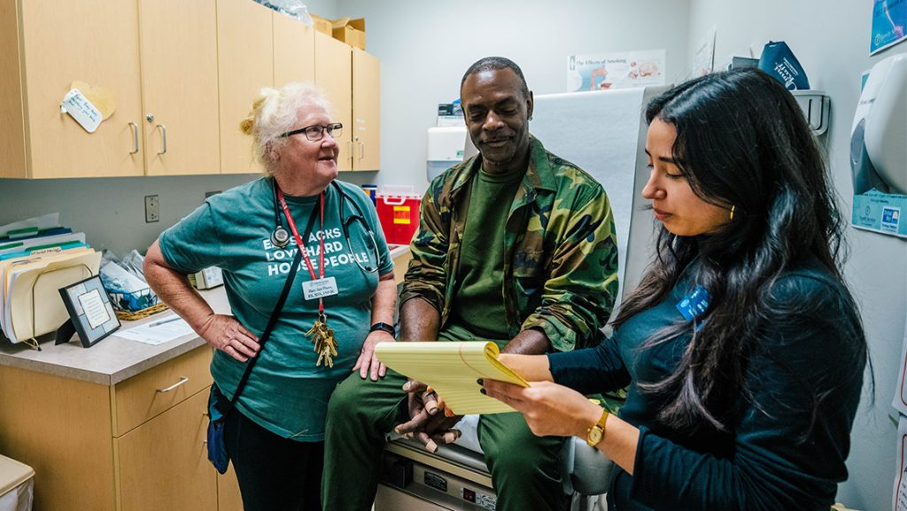 A UNCG genetic counseling student talks to a man in an examination room.
