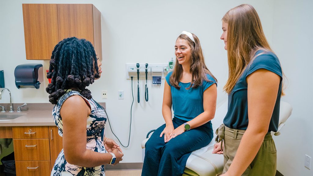 UNCG students chat on a physical exam table.