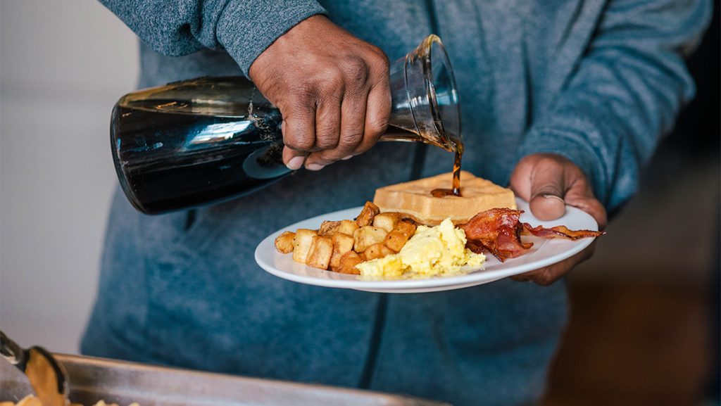 A person drizzles syrup over a plate of waffles.