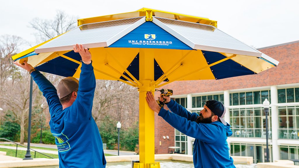 UNCG employees install a solar-powered table umbrella.