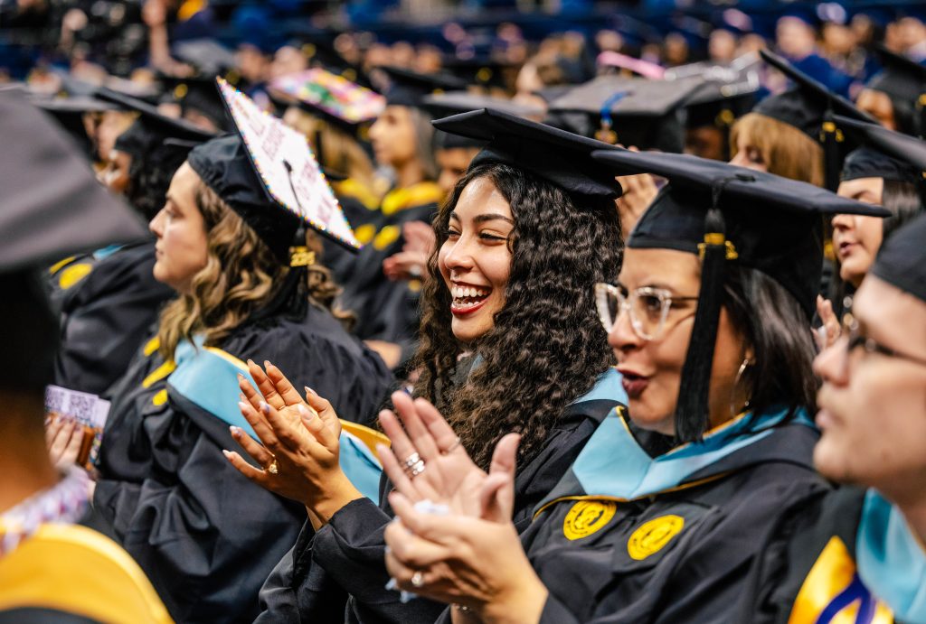 Seated master's grads clap at commencement.