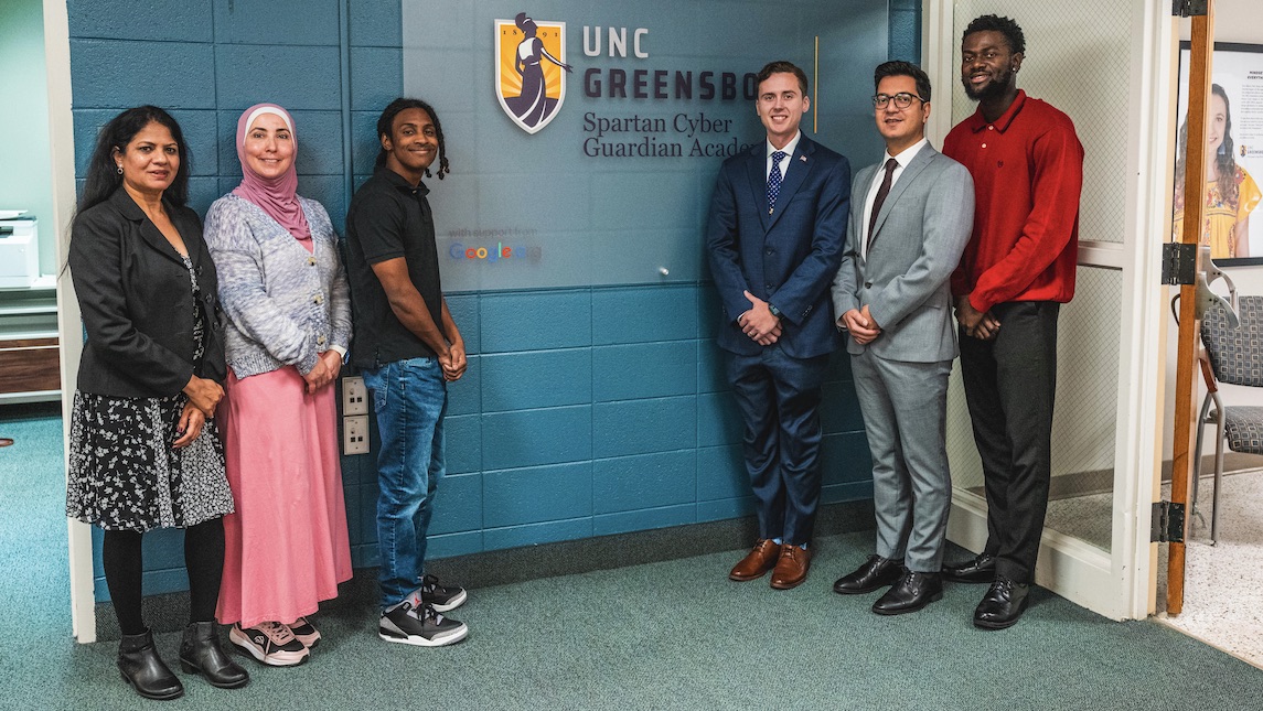 UNCG Spartan Cyber Guardian Academy students and professors pose in front of sign.