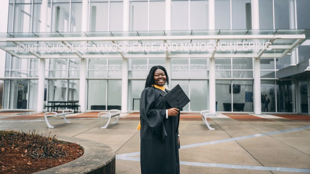JSNN graduate Patience Kwara poses outside of the JSNN building in her cap and gown.
