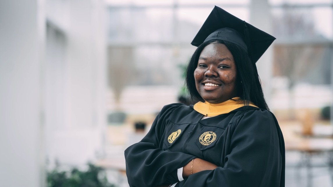 JSNN graduate Patience Kwara poses inside the JSNN building in her cap and gown.