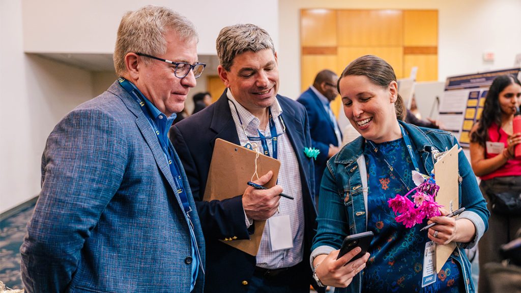 UNCG Dean Carl Mattacola looks at something on the phone shared by Erin Reifsteck and alumnus Dale Phipps ’82.