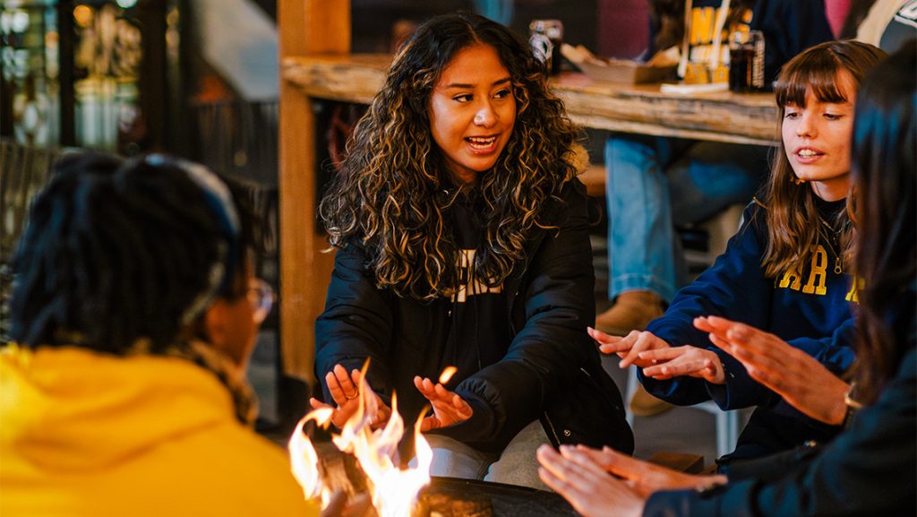 UNCG students sit around a small fire.