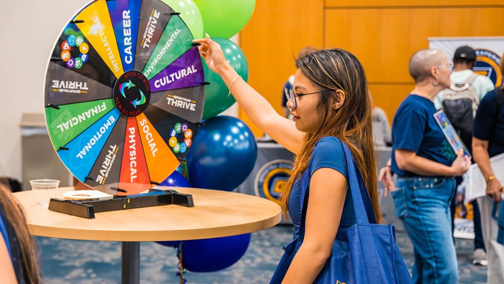 A UNCG student spins a wellness wheel at an event.