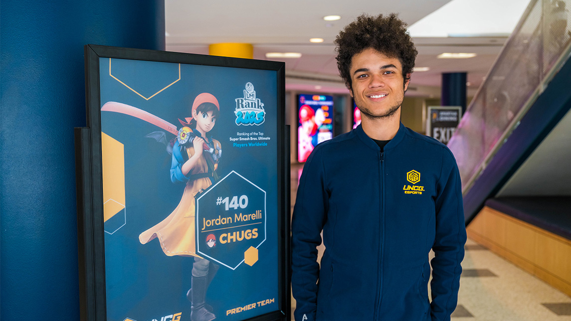 Jordan Marelli next to a poster showing his Smash ranking out UNCG Esports Arena.