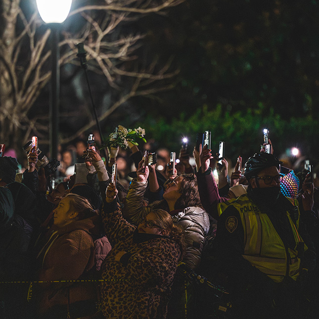 Crowd of people gathered in the dark holding phones up.