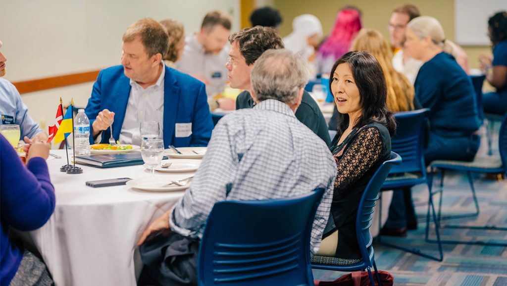 UNCG faculty chat during a meal at a table with flags of other countries.