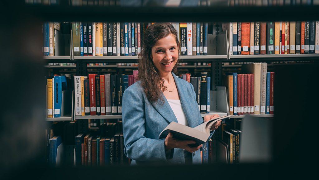 UNCG Honors College Dean Kimberly Petersen peering through a bookshelf.