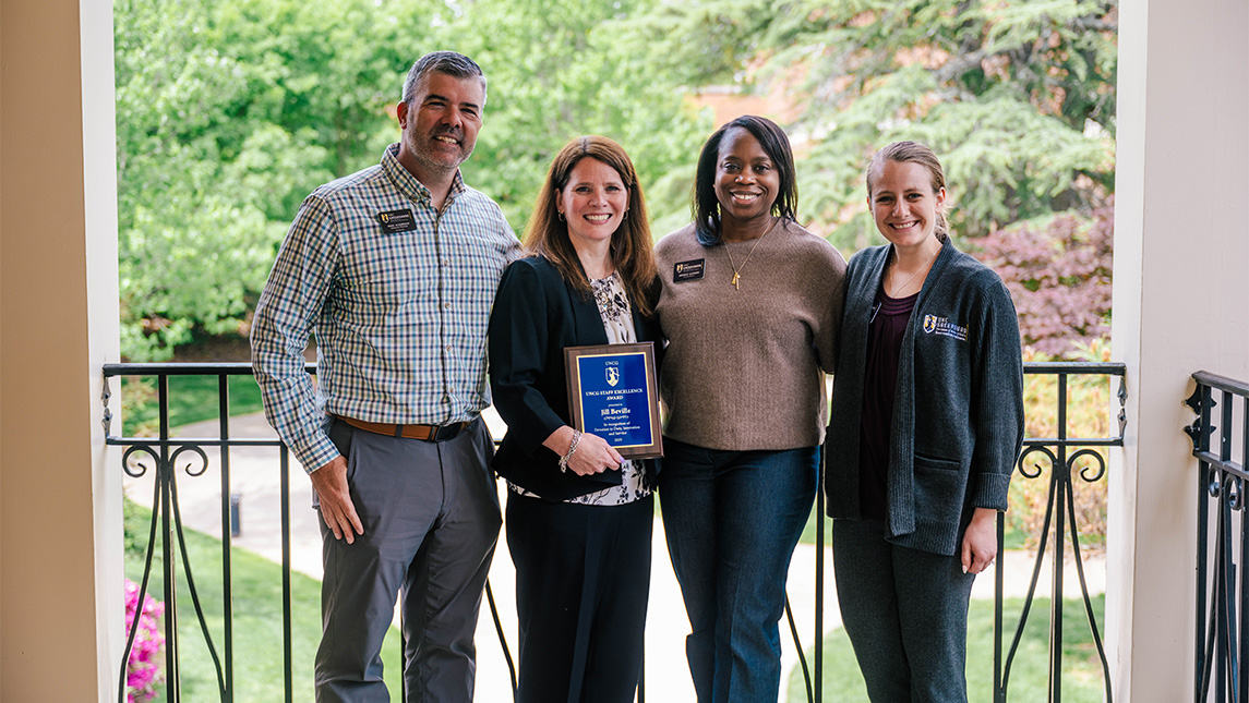 Four UNCG staff members and friends show off an award.