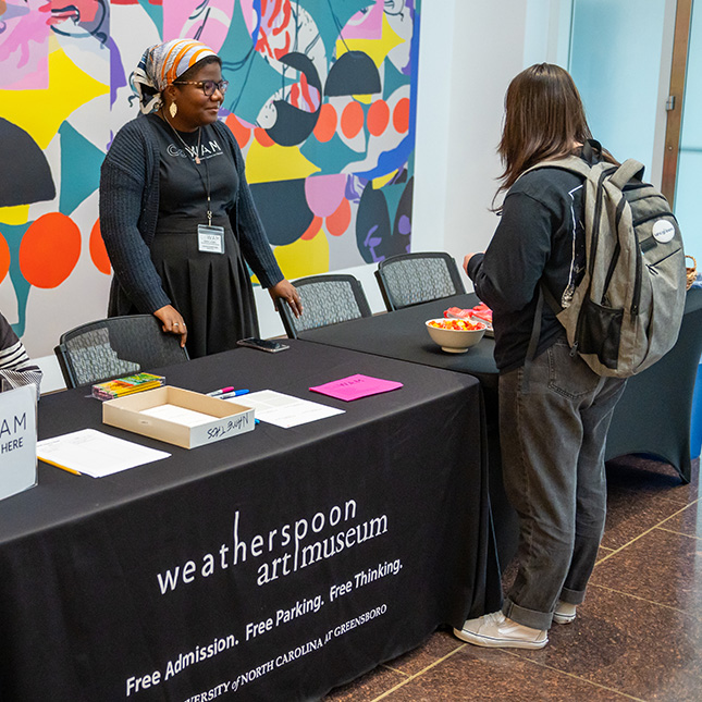 Student with a backpack checks in at a desk at the Weatherspoon Art Museum. 