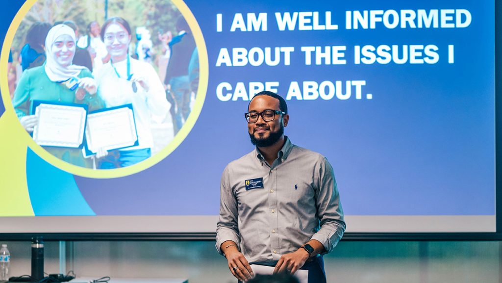 Man addresses a classroom in front of a screen that says "I am well informed about the issues I care about."