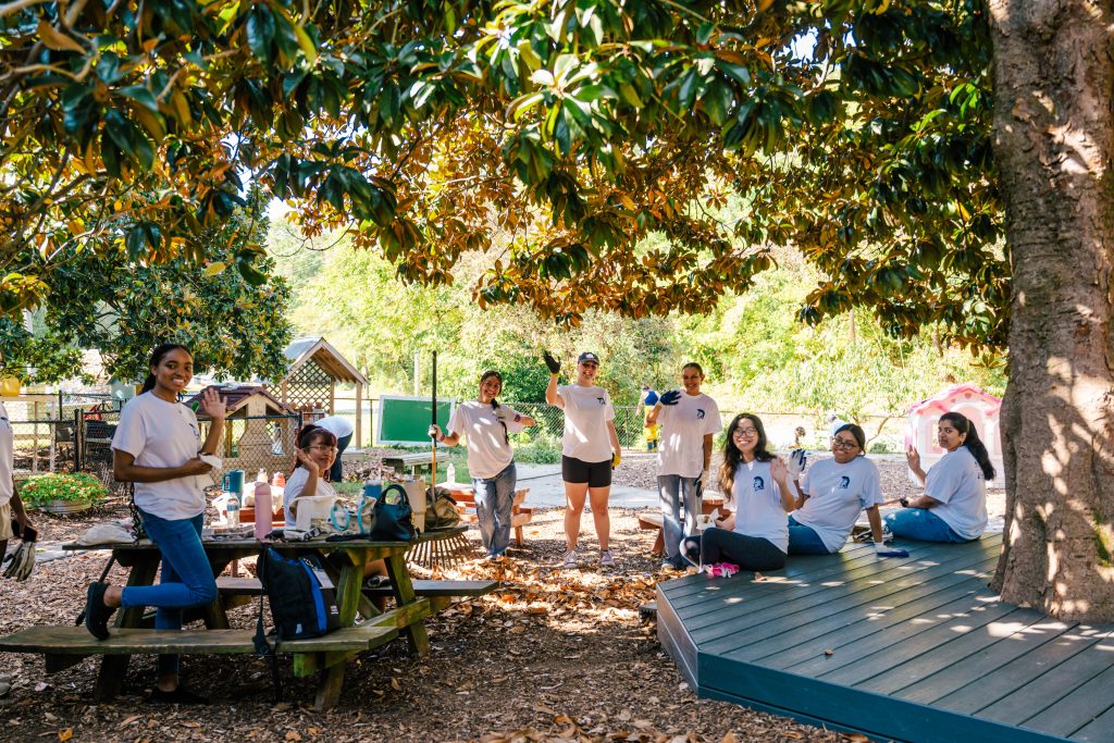 A group of students in matching t-shirts pose in a playground they are working to clean up.
