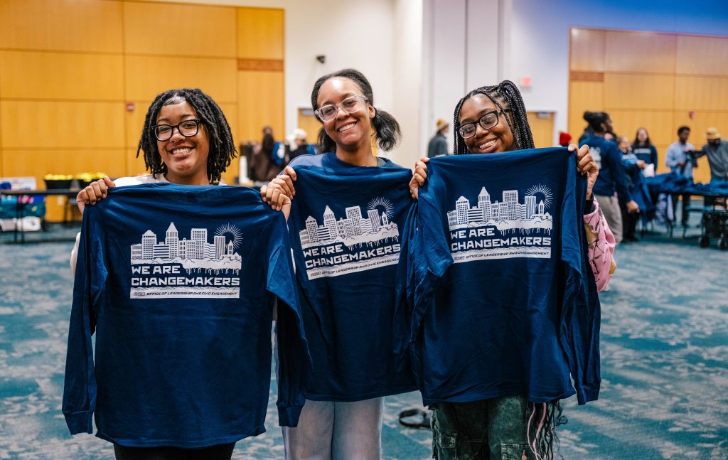 Three students hold changemaker t-shirts.