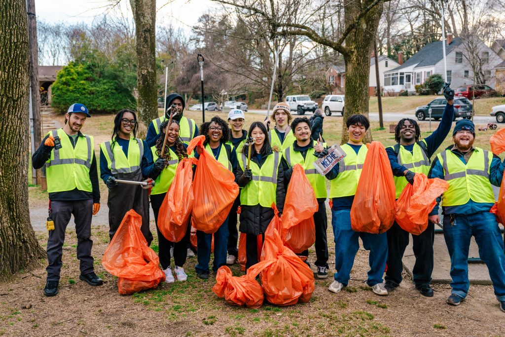 A group of students pose together outside with reflective vests and trashbags.