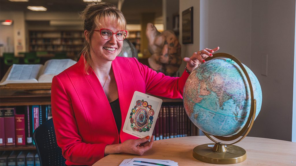 UNCG MLIS student H. Blake-Lee points at a globe.