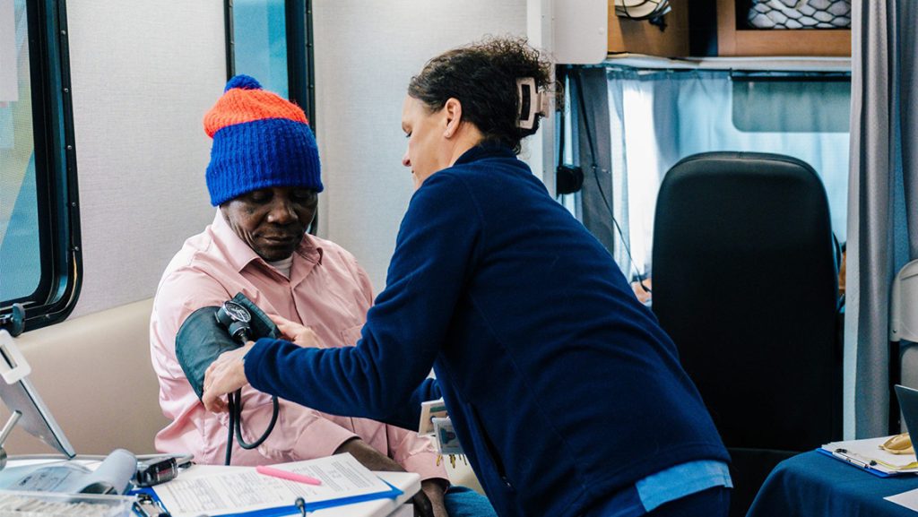 UNCG nursing student checks a man's blood pressure inside Minerva Mobile Health unit.