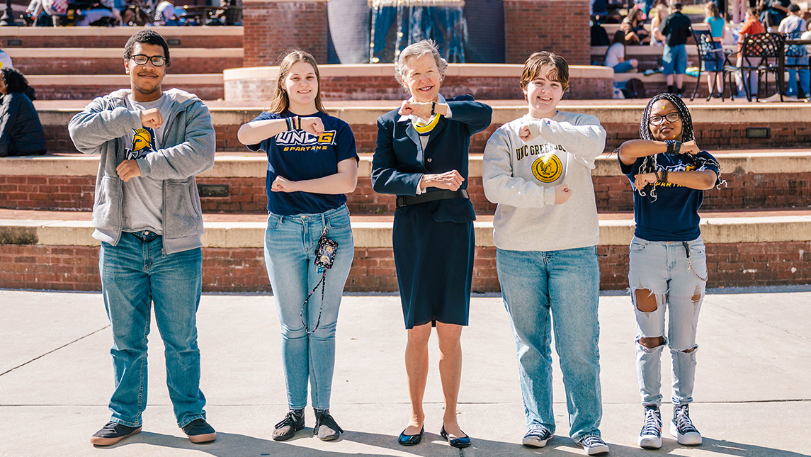 Four UNCG students and a faculty member form the G at Moran Commons Plaza.