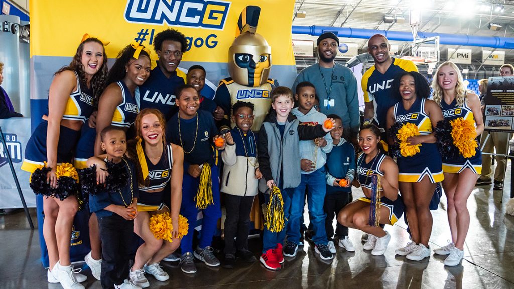 UNCG cheerleaders with mascot Spiro pose with kids at basketball court.