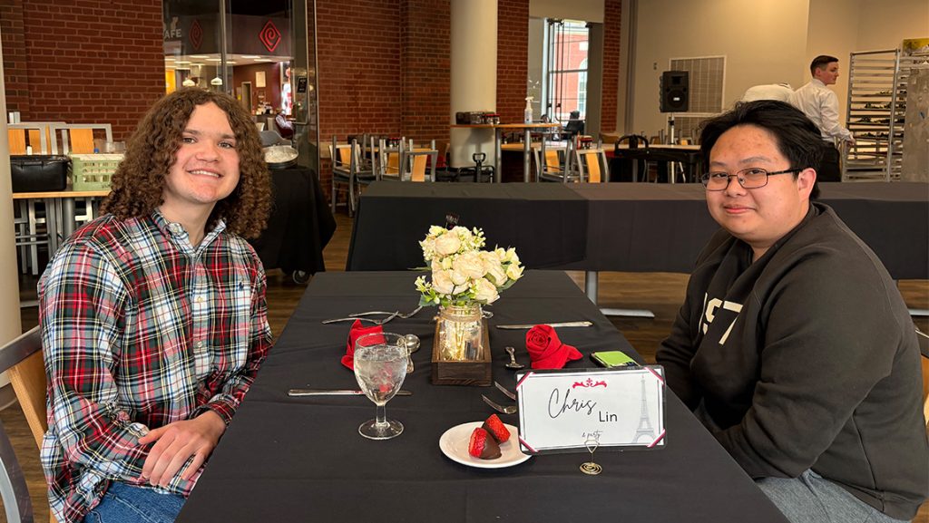 Students sit together at a table with flowers and tablecloth.