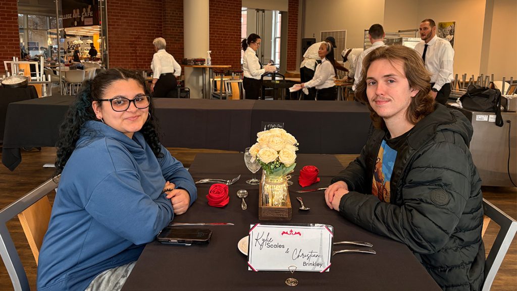 Students sit together at a table with flowers and tablecloth.