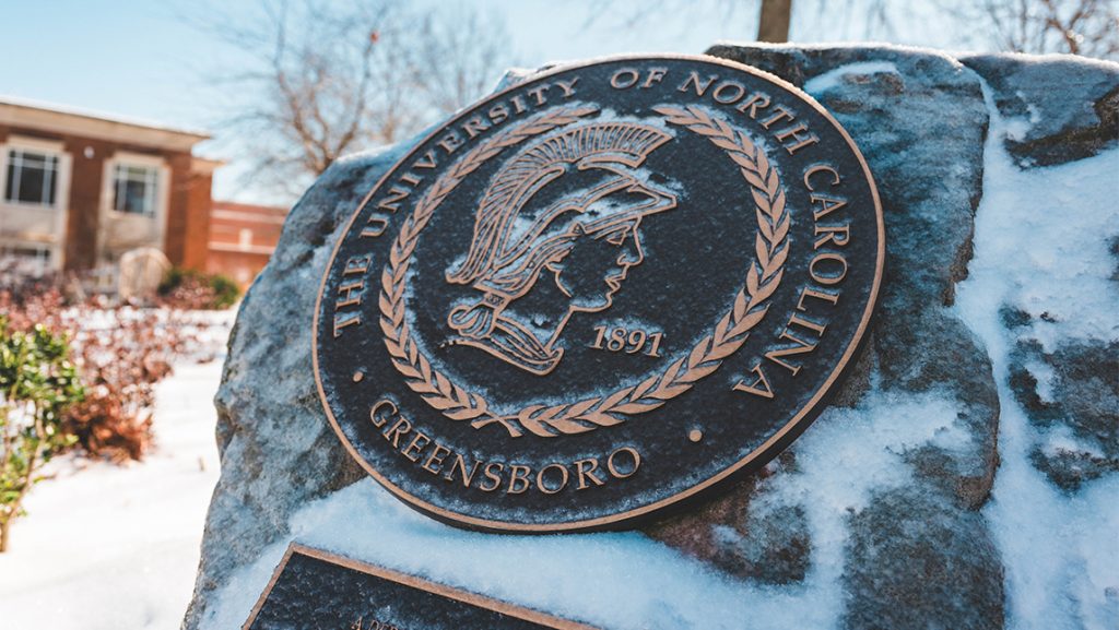 UNCG seal on a snow-covered rock.