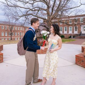 A UNCG student gives a bouquet of daisies to another.