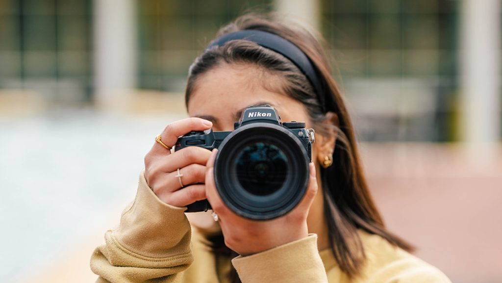 Close-up of a student on campus with a camera pointed at you.
