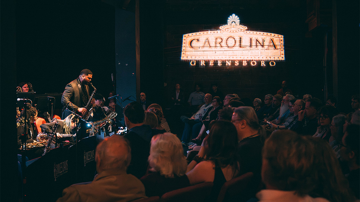 Audience listens to UNCG student Franco Romero playing the saxophone.