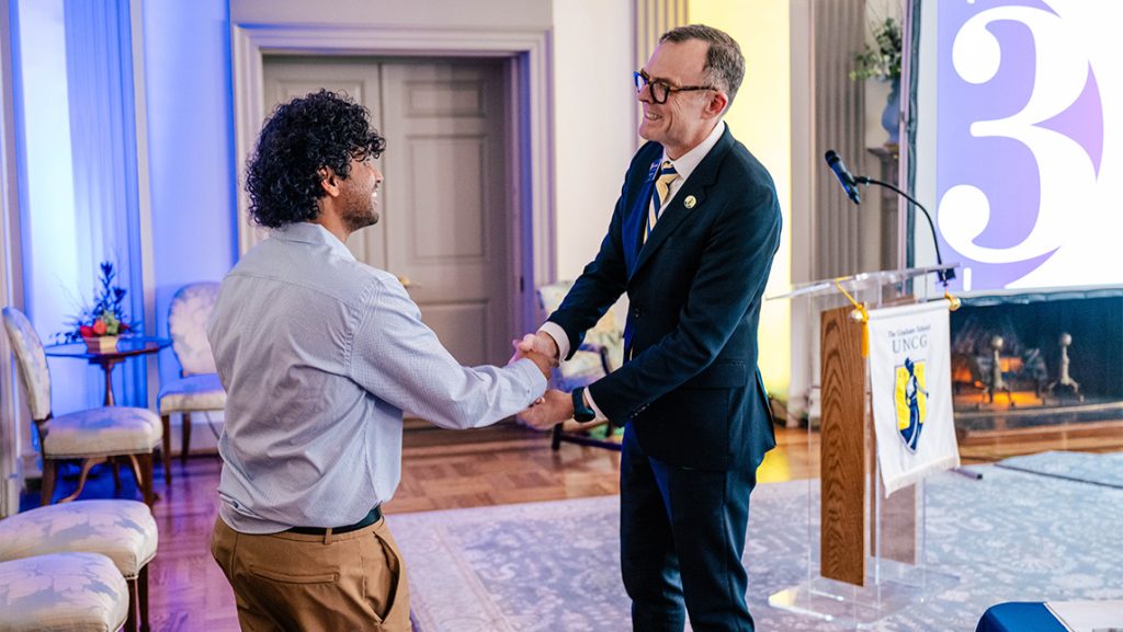 UNCG Graduate School Dean Greg Bell shakes hands with Praveen Pasupathi.