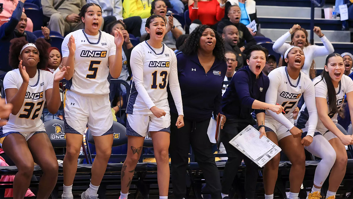 UNCG women's basketball players cheer from the sidelines.