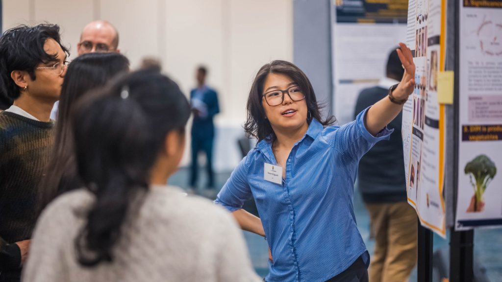 A student presents her research poster to a group of attendees